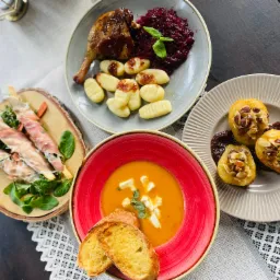 Kompozycja czterech talerzy z różnymi potrawami: pieczona kaczka z modrą kapustą i gnocchi, roladki z szynki parmeńskiej na grzankach, krem z dyni z grzankami i serem oraz pieczone gruszki...