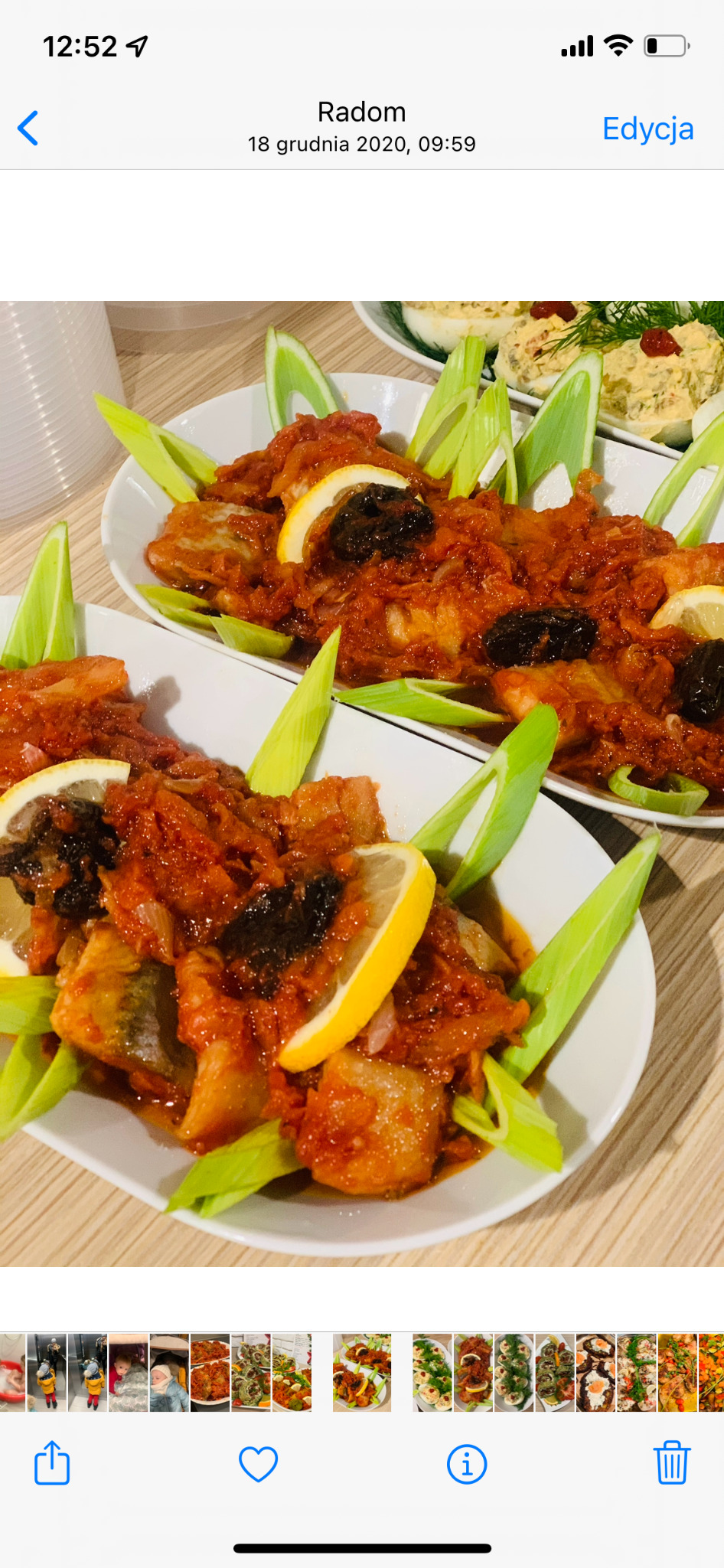 Dwa białe talerze z rybą w sosie pomidorowym, udekorowane plasterkami cytryny i pędami cebuli, na drewnianym stole. W tle jajka faszerowane.