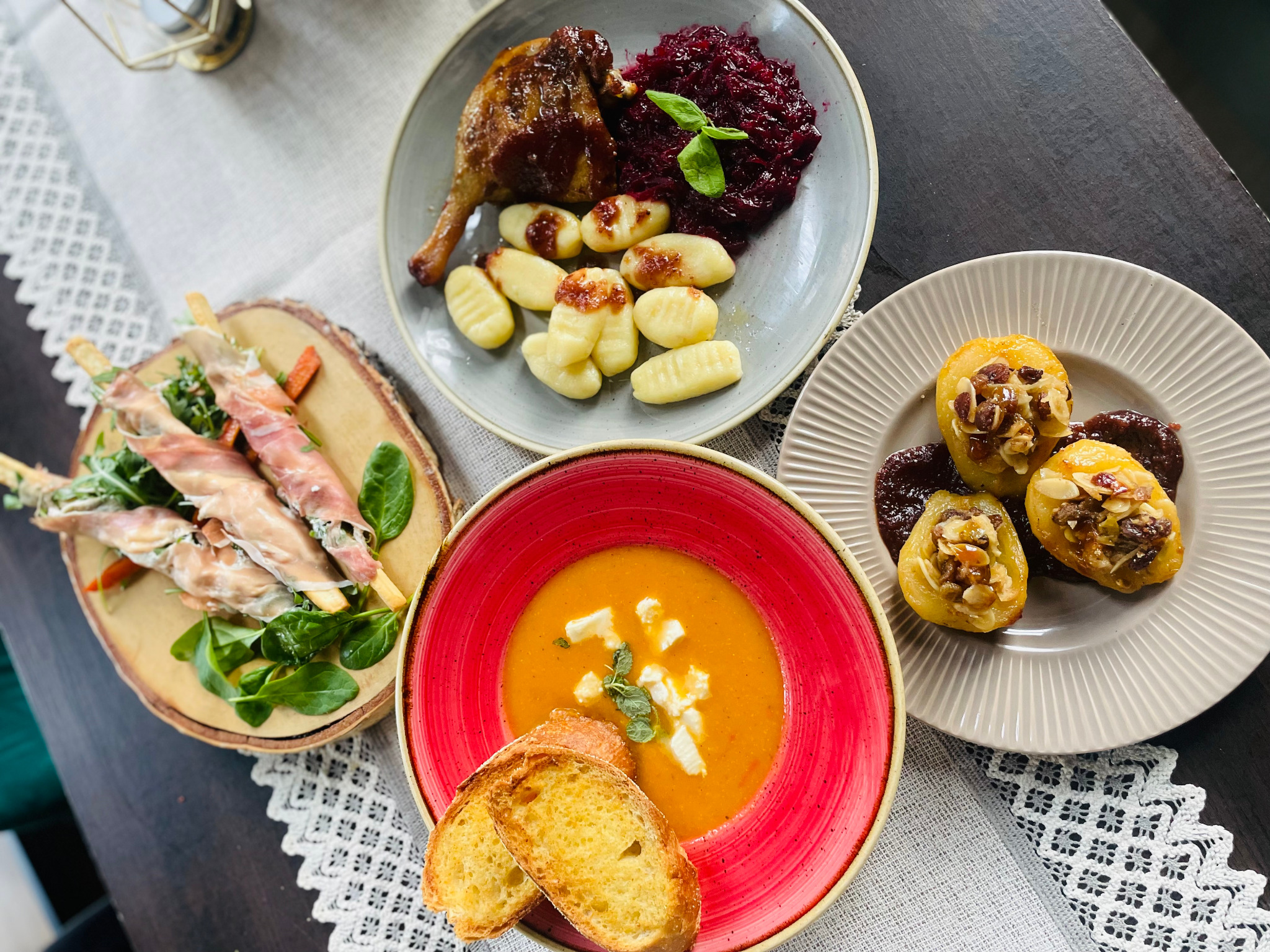 Kompozycja czterech talerzy z różnymi potrawami: pieczona kaczka z modrą kapustą i gnocchi, roladki z szynki parmeńskiej na grzankach, krem z dyni z grzankami i serem oraz pieczone gruszki...