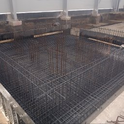 Marek Rauba Konstrukcje - Siatka zbrojeniowa fundamentu w wykopie, widoczny pracownik w tle, przygotowana do zalania betonem.