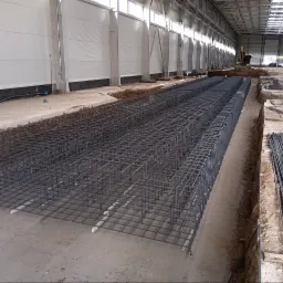 Siatka zbrojeniowa fundamentów ułożona w wykopie na hali, widoczne białe elementy dystansowe pod zbrojeniem oraz równe ułożenie prętów.