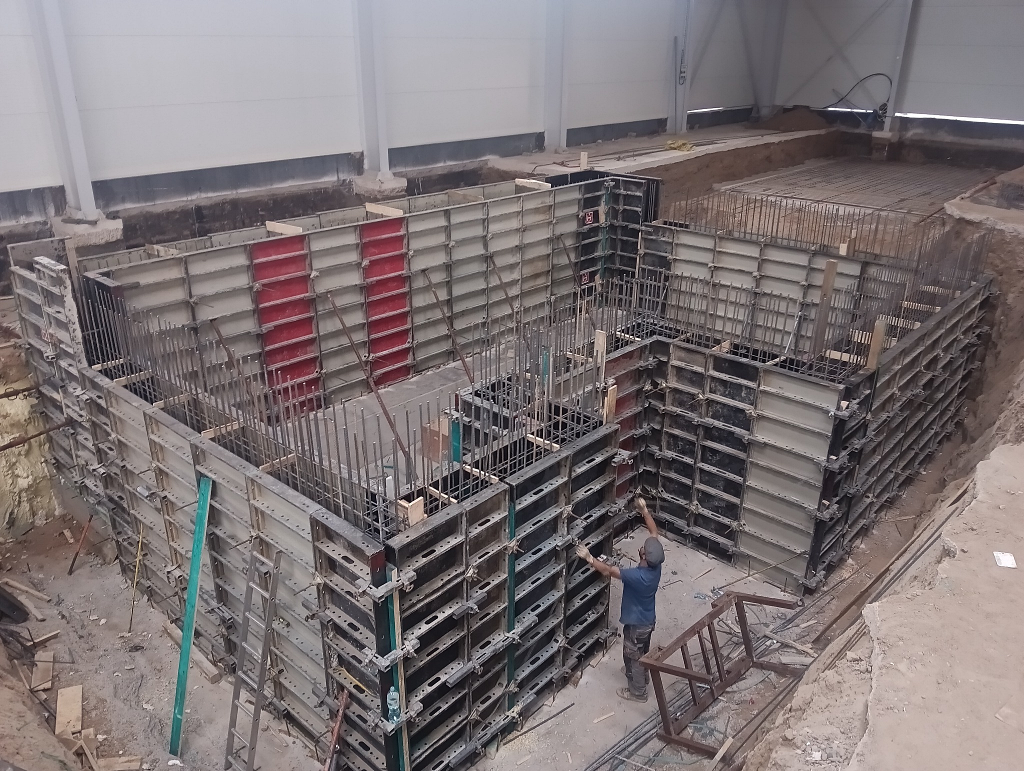 Montaż szalunków i zbrojenia pod fundament budynku przemysłowego, widok z góry na wykop z pracującym robotnikiem.