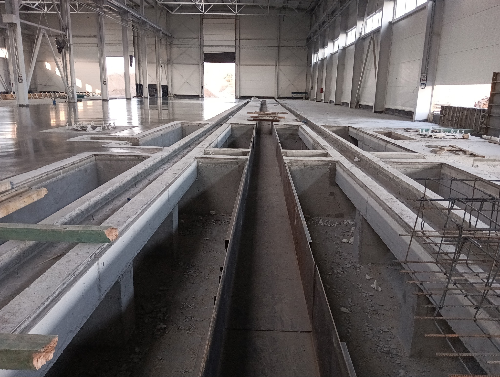 Wnętrze hali produkcyjnej w Gołdapi z przygotowanymi fundamentami pod maszyny i instalacje, widoczne zbrojenia i betonowe wylewki.