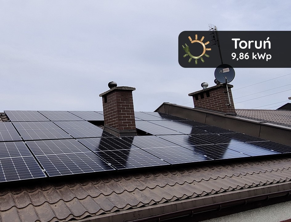 Panele fotowoltaiczne na brązowym dachu domu jednorodzinnego w Toruniu, z kominem z cegły i anteną satelitarną, moc instalacji 9.86 kWp.