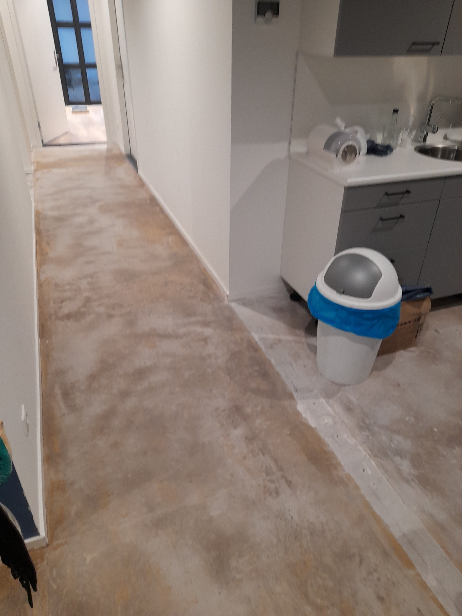 Przygotowanie podłoża pod wylewkę: szlifowany beton w korytarzu, widoczny śmietnik i fragment szafek kuchennych w tle.