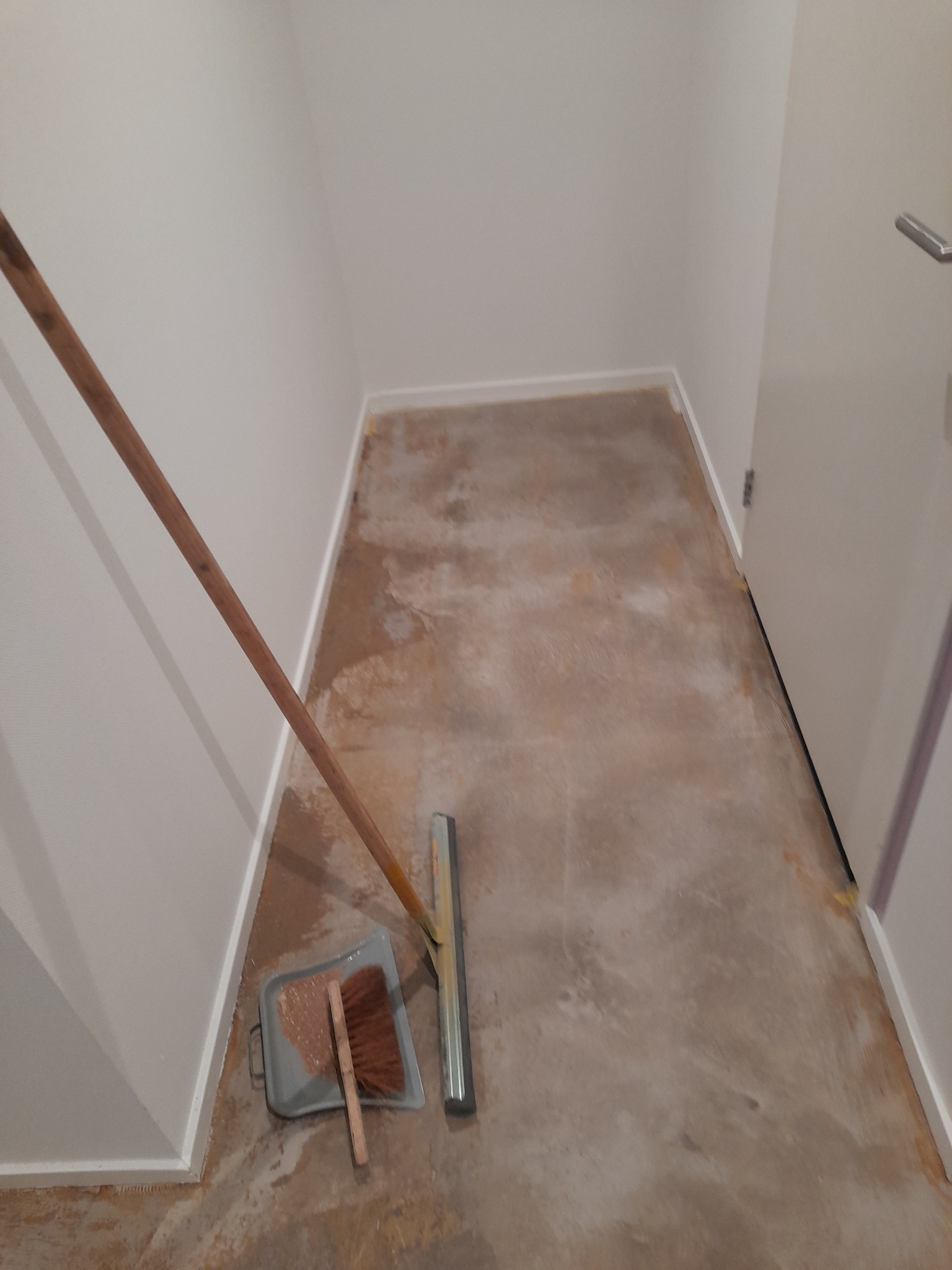 Przygotowanie podłoża: oczyszczona posadzka w pomieszczeniu z widocznymi narzędziami - miotłą, szufelką i zgarniaczem.