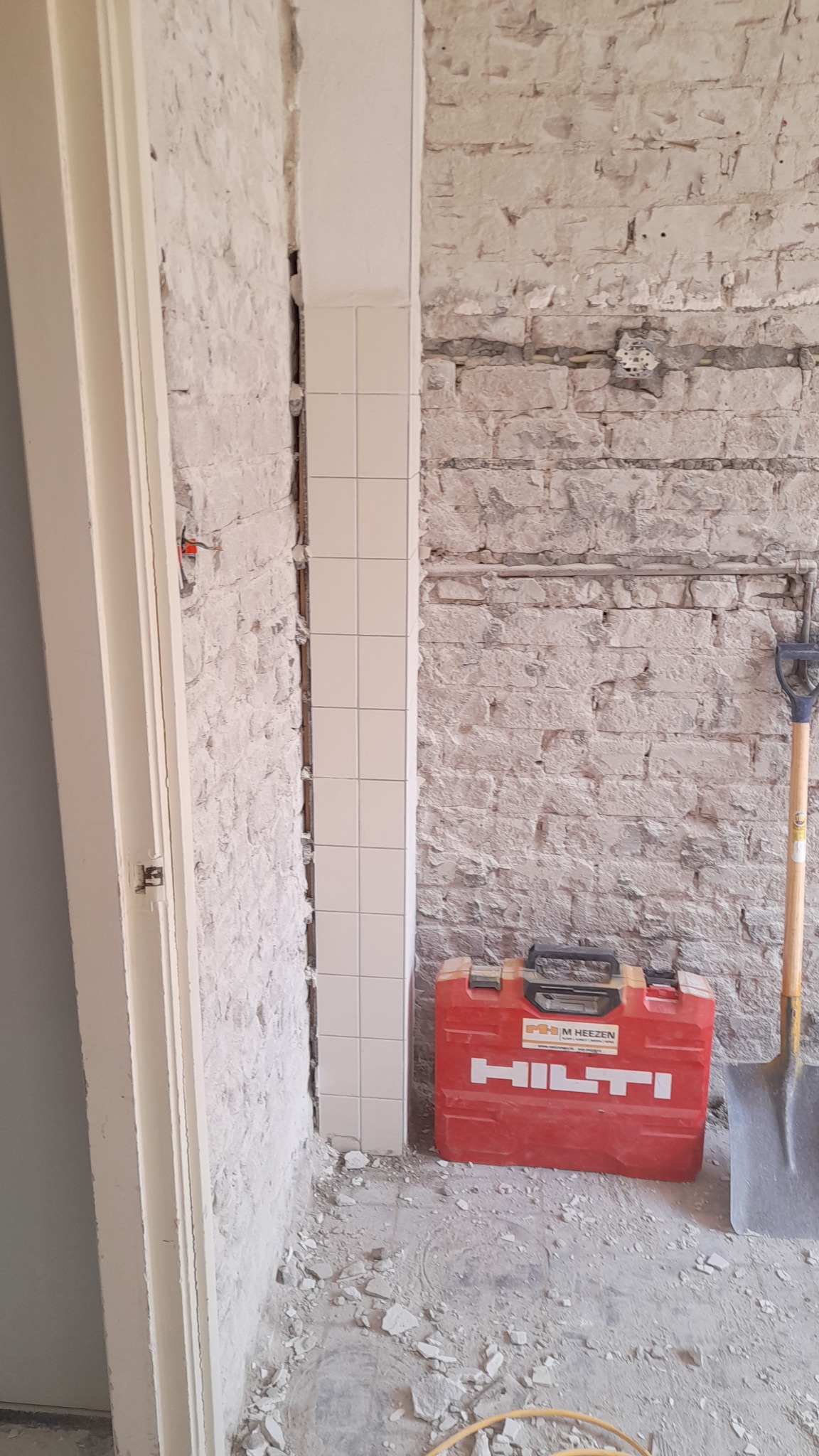 Fragment ściany z usuniętymi płytkami w trakcie prac remontowych w Eindhoven, widoczny czerwony kufer narzędziowy firmy Hilti i łopata.