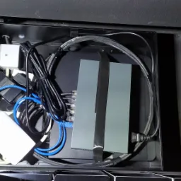 Otwarta szafka instalacyjna z routerem, zasilaczami i okablowaniem w kolorach czarnym i niebieskim, widok z góry.