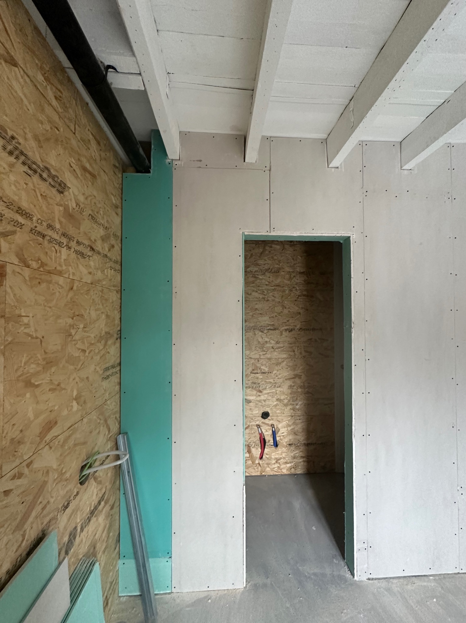 Wnętrze w trakcie prac wykończeniowych: ściany z płyt kartonowo-gipsowych, widoczne drewniane belki stropowe, instalacja elektryczna i hydrauliczna w ścianie z OSB, przygotowanie do dalszych etapów...