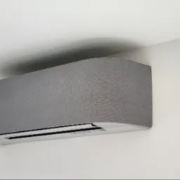 Szary klimatyzator ścienny z teksturowaną obudową w nowoczesnym wnętrzu z białymi ścianami.