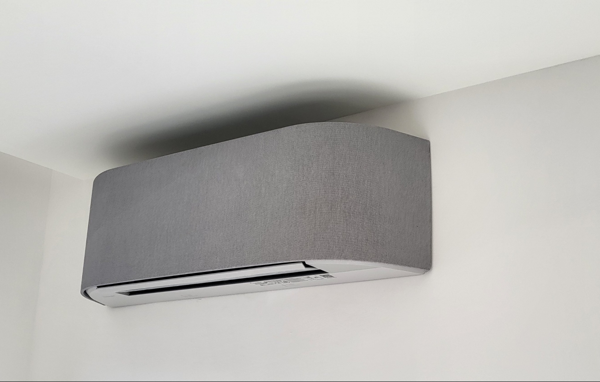 Szary klimatyzator ścienny z teksturowaną obudową w nowoczesnym wnętrzu z białymi ścianami.