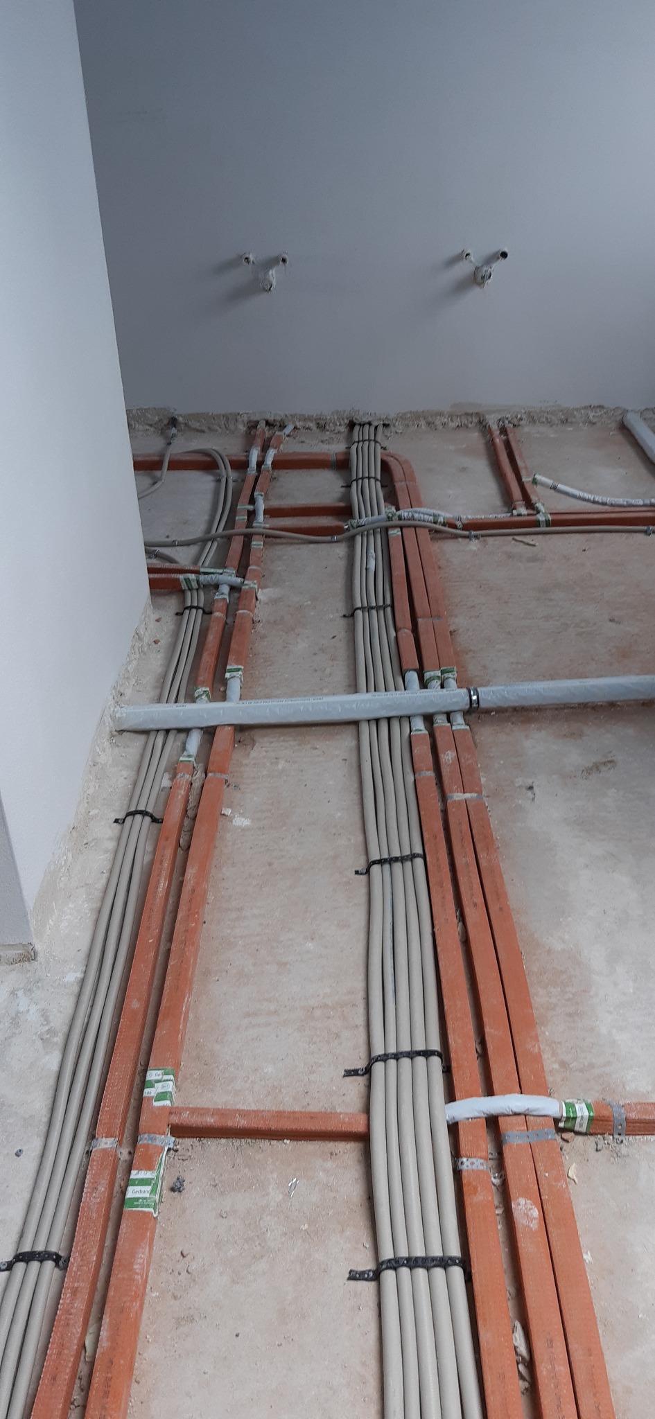 Układanie przewodów elektrycznych w peszlach, mocowanych do podłoża za pomocą pomarańczowych profili, przed wylaniem posadzki.