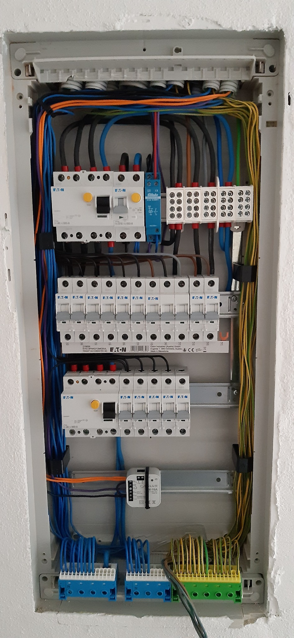 Rozdzielnica elektryczna z zainstalowanymi bezpiecznikami Eaton, zabezpieczeniami różnicowoprądowymi, listwami zaciskowymi i okablowaniem w kolorach: czarnym, niebieskim, pomarańczowym...