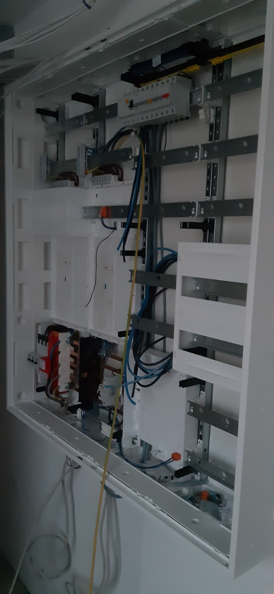 Otwarta biała skrzynka rozdzielcza z zamontowanymi elementami elektrycznymi, widoczne kable w różnych kolorach oraz szyny montażowe.