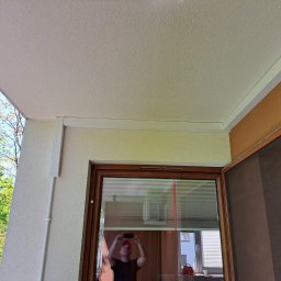 ICEKLIMA - Biała listwa maskująca klimatyzację na balkonie, widoczny kabel zasilający i otwarte okno z moskitierą.