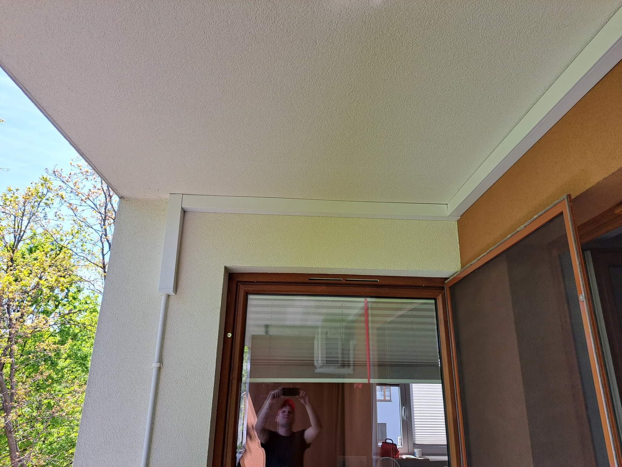 Biała listwa maskująca klimatyzację na balkonie, widoczny kabel zasilający i otwarte okno z moskitierą.