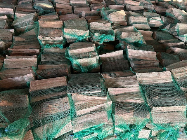 Stos worków z pociętym drewnem kominkowym, zapakowanym w zielone siatki, gotowym do transportu i użycia, widok z bliska.