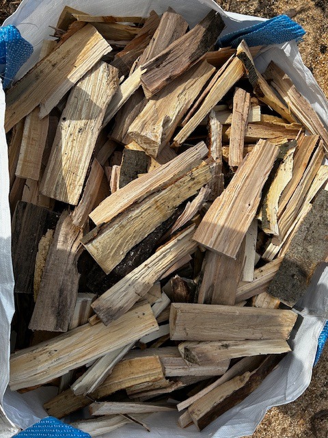 Worek wypełniony pociętym drewnem opałowym, widoczne naturalne słoje i kora. Kawałki ułożone nieregularnie, wystające poza krawędź worka.