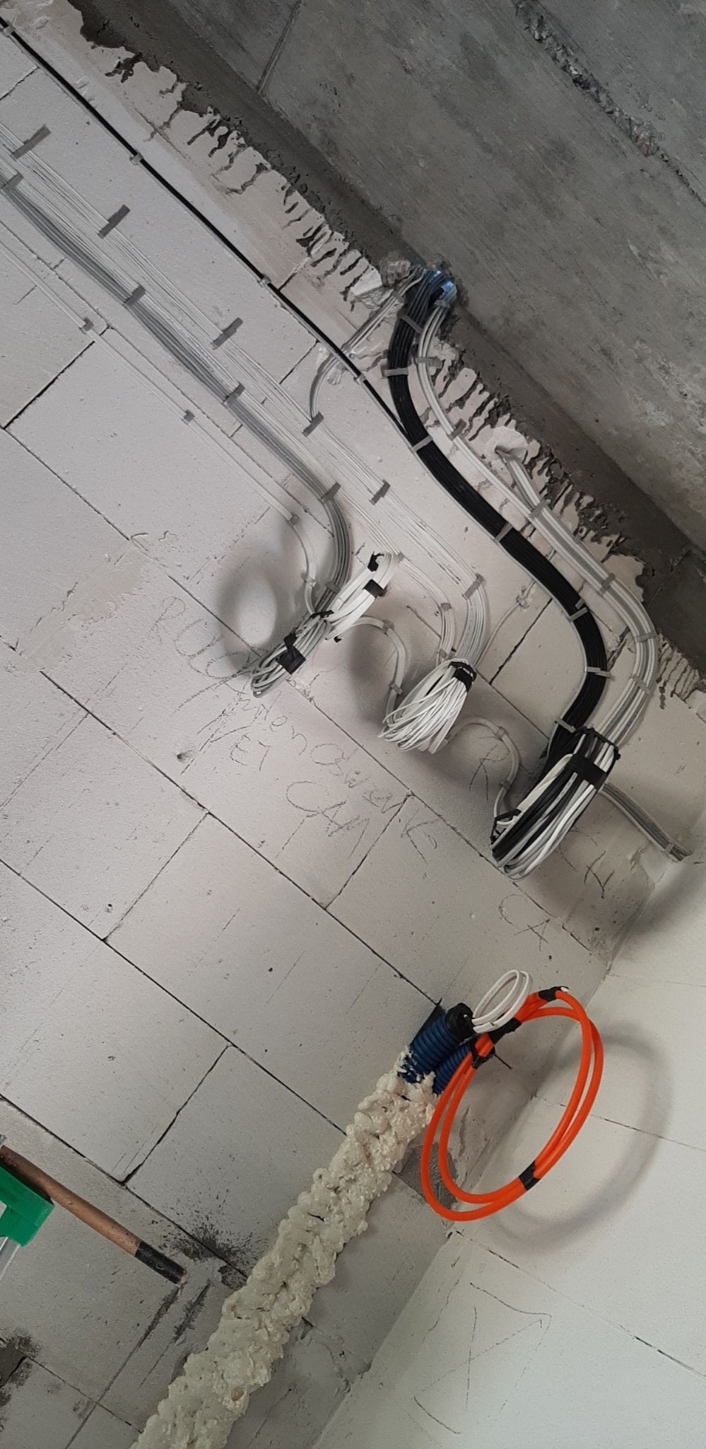 Układanie przewodów elektrycznych w peszlu na surowym murze z betonu komórkowego, widoczne kable w różnych kolorach i grubościach, mocowane do ściany za pomocą uchwytów, z fragmentami pianki...