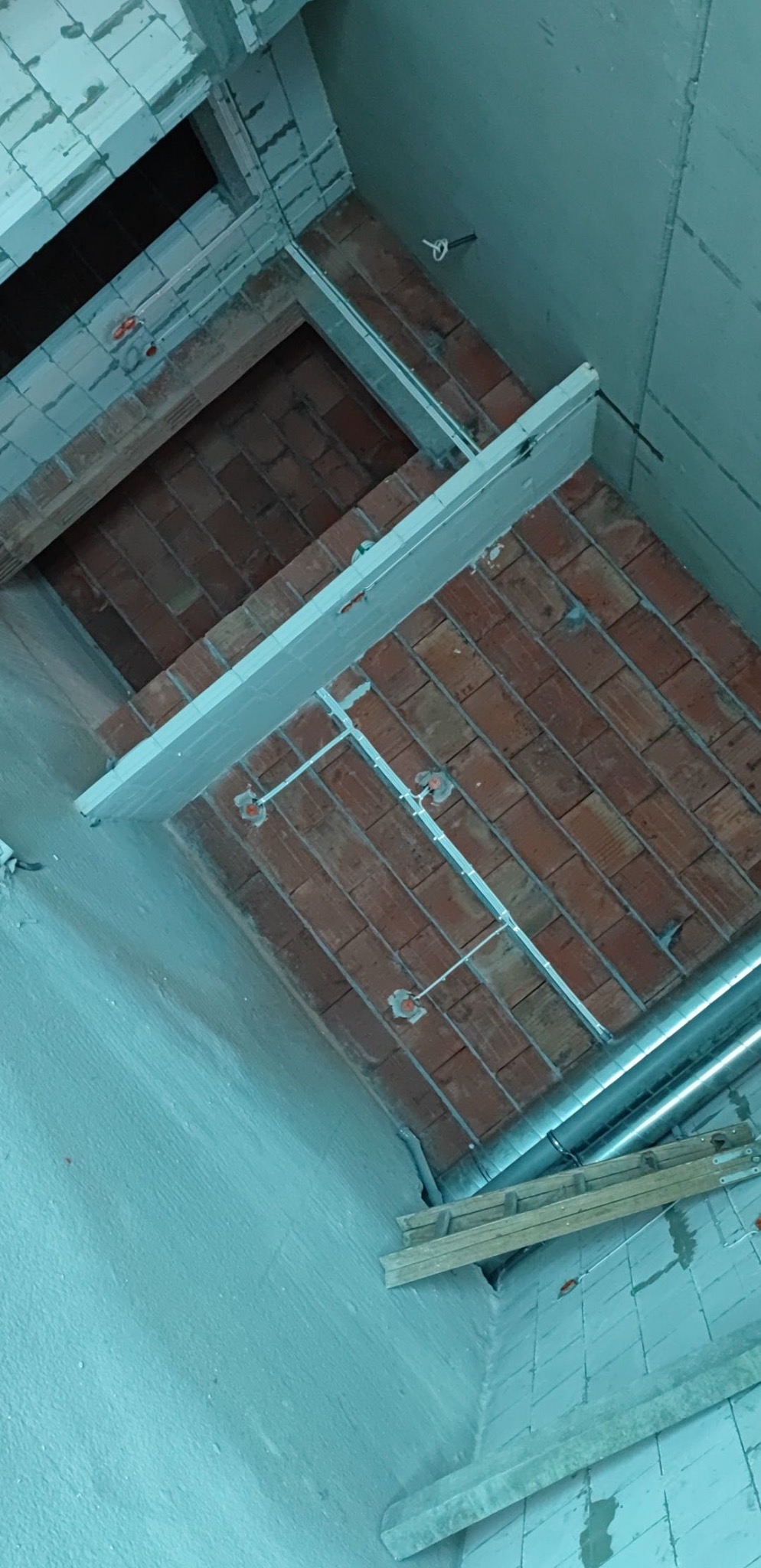 Instalacja elektryczna w trakcie montażu pod ceglanym stropem, widoczne przewody w metalowych listwach i puszki instalacyjne, fragment drabiny i rury wentylacyjnej w tle.