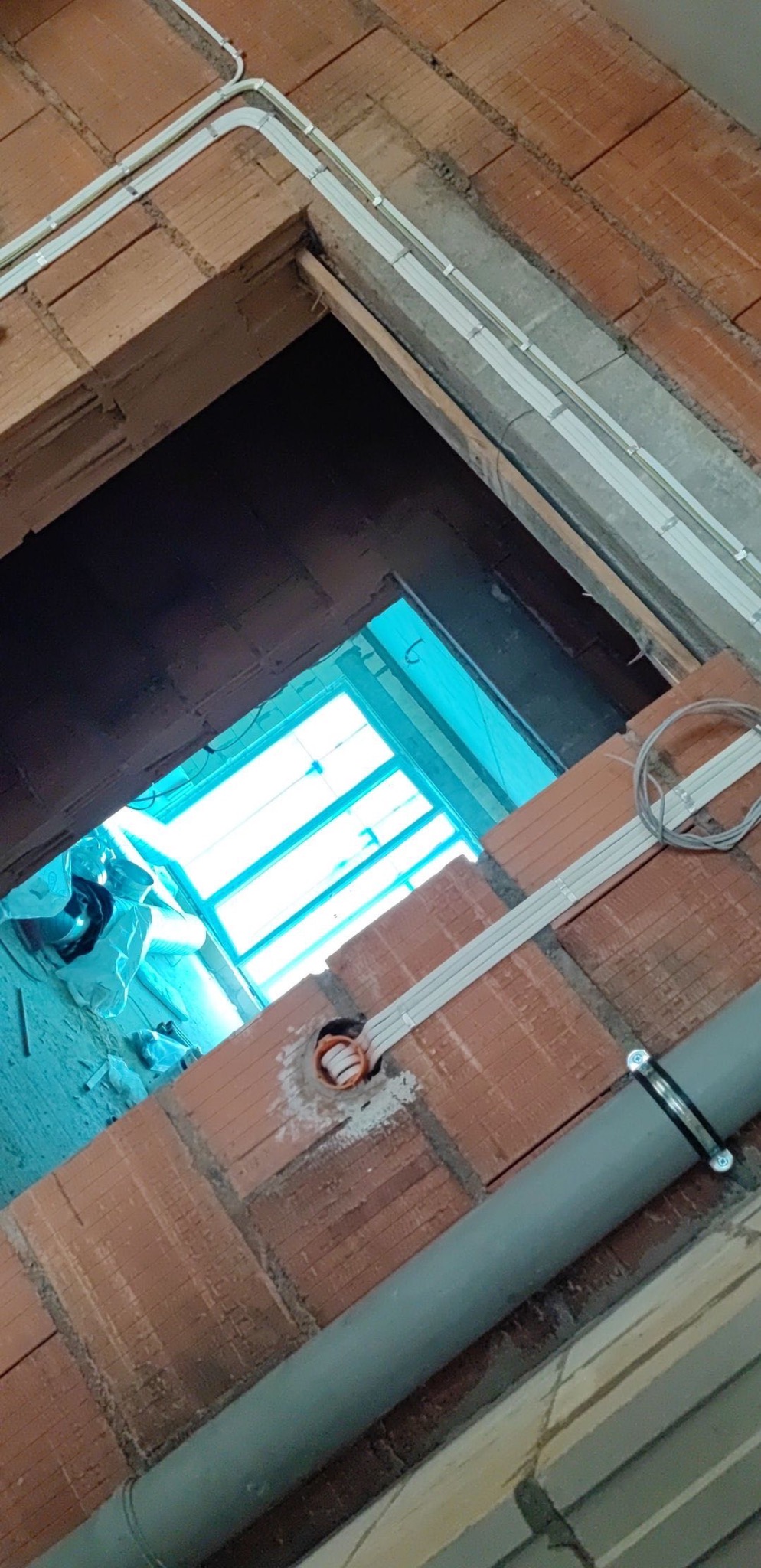 Wewnętrzne okablowanie elektryczne w peszlach, prowadzone wzdłuż surowego muru z cegły dziurawki, z widocznym otworem pod gniazdko.