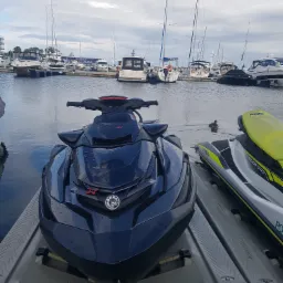 Czarny skuter wodny SeaDoo z kroplami wody na lakierze, zaparkowany w marinie Yacht Park Gdynia, z widokiem na zacumowane jachty i żaglówki.