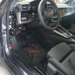 Wnętrze Audi A3 z demontowanymi elementami deski rozdzielczej i osłonami, widoczne narzędzia (wkrętak, podważki) na dywaniku, odsłonięta skrzynka bezpieczników.