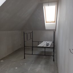 Robgaw - Poddasze w trakcie przygotowania do malowania: ściany wyszpachlowane, okno dachowe, rusztowanie z kielnią na drewnianym podeście, surowy beton na podłodze.