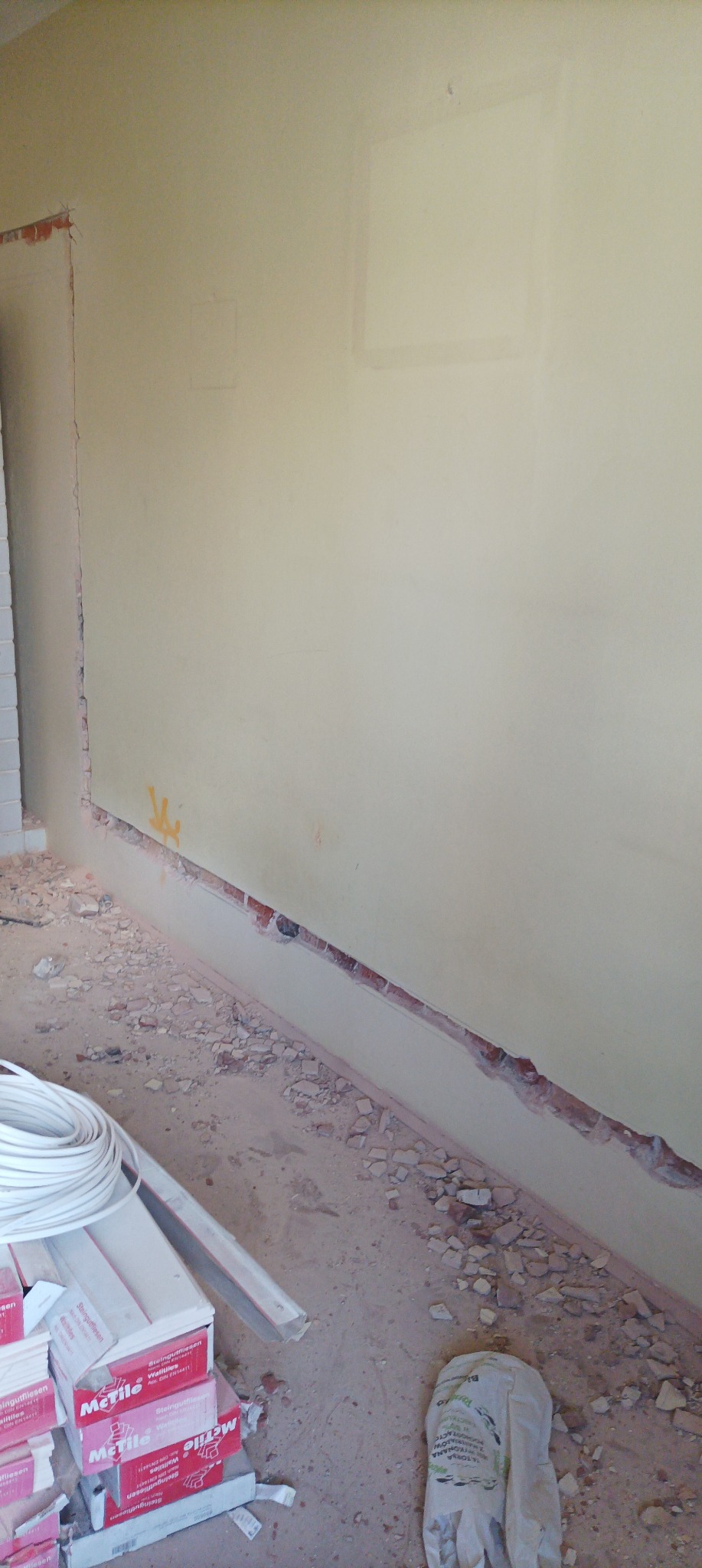 Ściana z wyciętym fragmentem pod instalację elektryczną, widoczne przewody i puszki elektryczne w kartonach na podłodze pokrytej gruzem.