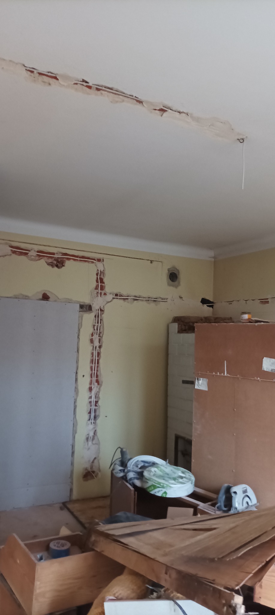 Wnętrze w trakcie remontu: odkryte przewody elektryczne w bruzdach na ścianie, fragmenty starej instalacji, narzędzia i materiały budowlane w nieładzie.