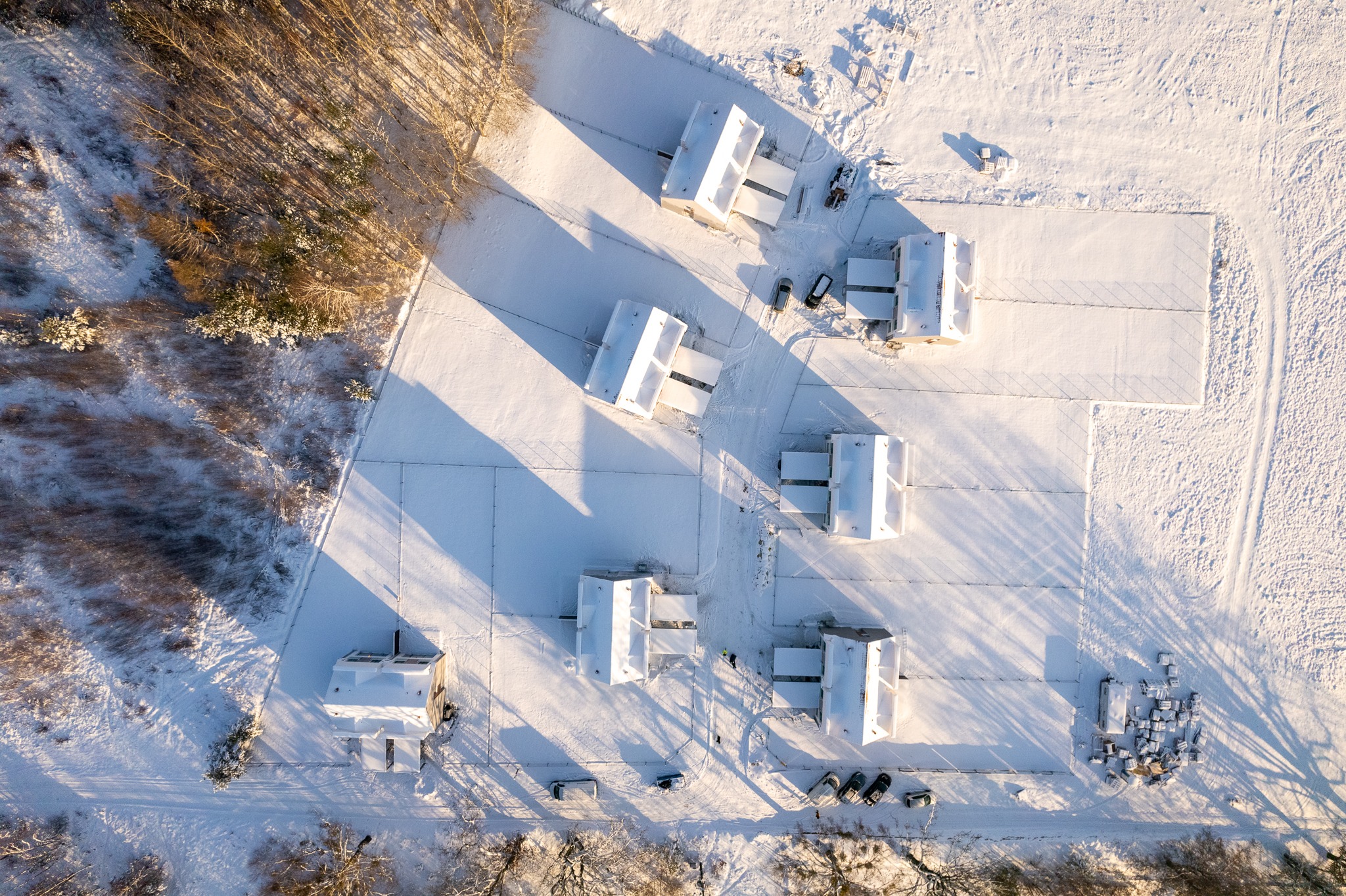 Zimowy widok z lotu ptaka na osiedle domów jednorodzinnych pokrytych śniegiem, z widocznymi samochodami i drzewami.