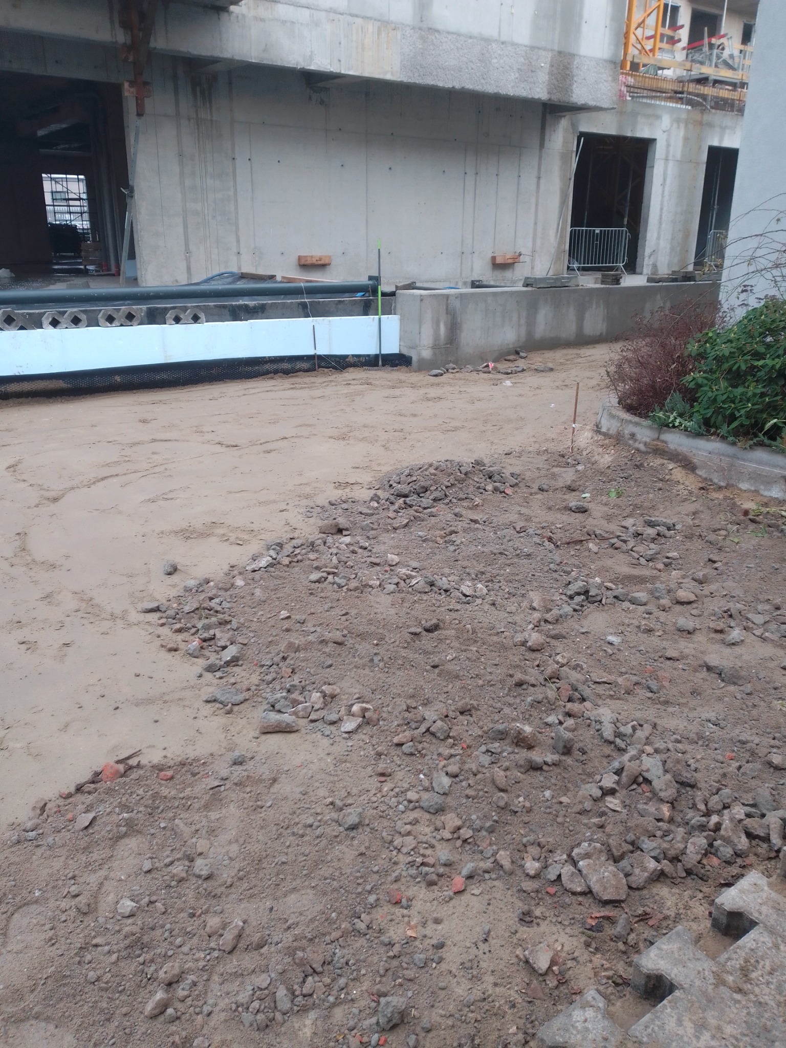 Teren przygotowany pod budowę, widoczne fundamenty budynku w stanie surowym, piasek, gruz i materiały izolacyjne