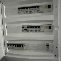 IEMS Instalacje Elektryczne Michał Sulich - Otwarta, biała skrzynka bezpiecznikowa z trzema rzędami wyłączników różnicowoprądowych i nadprądowych.