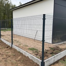 IEMS Instalacje Elektryczne Michał Sulich - Nowo zamontowane ogrodzenie panelowe z podmurówką betonową przylegające do budynku z elewacją w kolorze białym i grafitowym, widoczne ślady prac ziemnych.