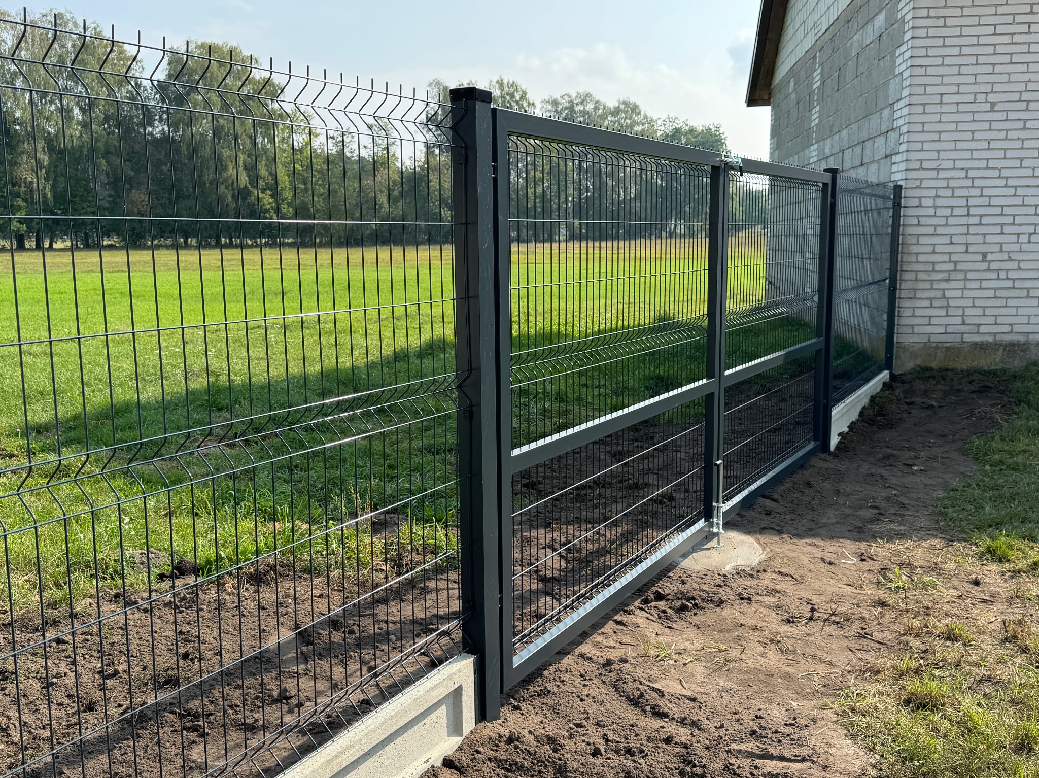 Nowoczesne ogrodzenie panelowe w kolorze antracytowym z podmurówką betonową, widok z zewnątrz posesji, trawnik w tle.