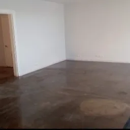 Pusty pokój z gładką, błyszczącą, brązową podłogą przypominającą żywicę epoksydową, białe ściany i framuga drzwi do innego pokoju w tle.