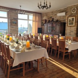 Złoty Taras Przysiersk Mieczysław Piotrowski - Uroczysta sala z długimi stołami nakrytymi białymi obrusami, zastawionymi talerzami, szklankami z sokiem pomarańczowym i dekoracjami kwiatowymi, oświetlona naturalnym światłem wpadającym przez duże...