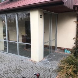 PRO MATYLDA GRAJKO - Montaż aluminiowej konstrukcji okiennej przy domu z narzędziami na zewnątrz. Widoczne ślady montażu i częściowo przeszklona fasada budynku.