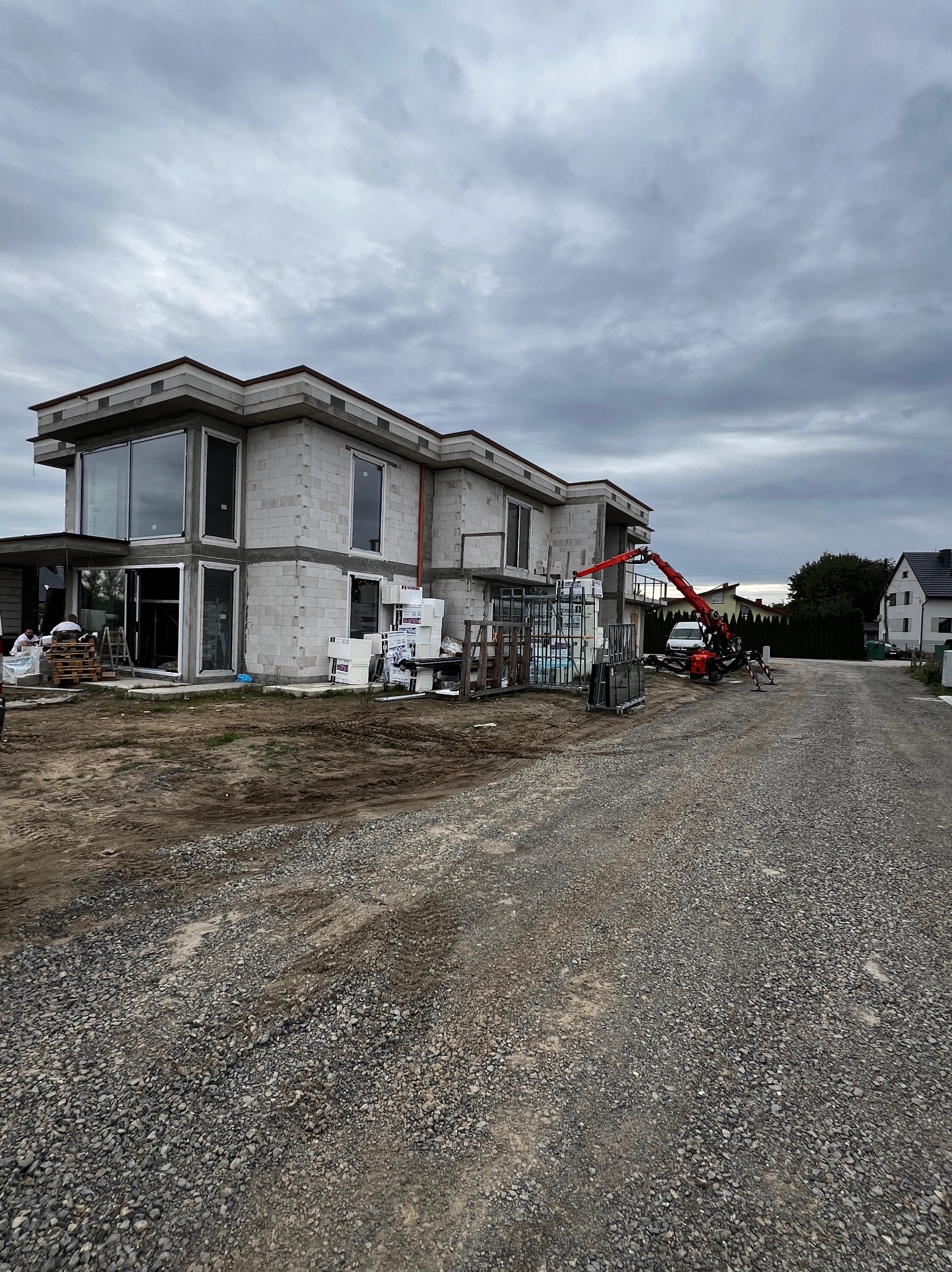 Budowa domu z betonu komórkowego w trakcie montażu okien. Na placu budowy stoi dźwig i materiały budowlane. Pochmurne niebo w tle.