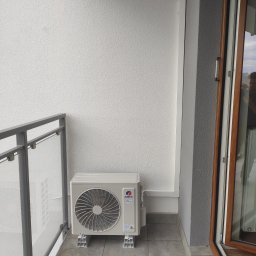 HeWa Paweł Świątkowski - Jednostka zewnętrzna klimatyzacji marki Gree zamontowana na balkonie, widoczna szara balustrada i brązowa rama okienna.