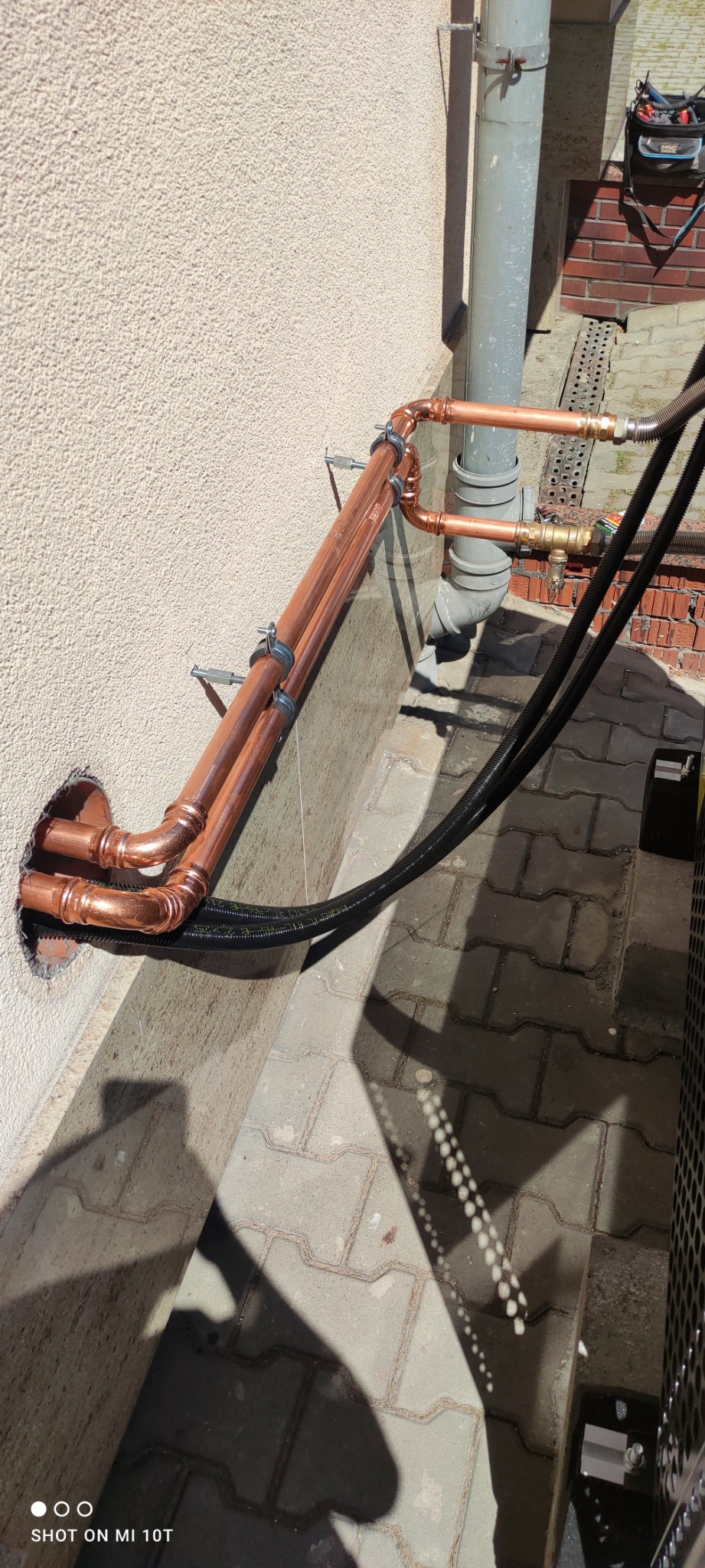 Miedziane rury instalacji grzewczej przymocowane do ściany budynku w Chorzowie, z widocznym otworem w elewacji i fragmentem instalacji zewnętrznej.