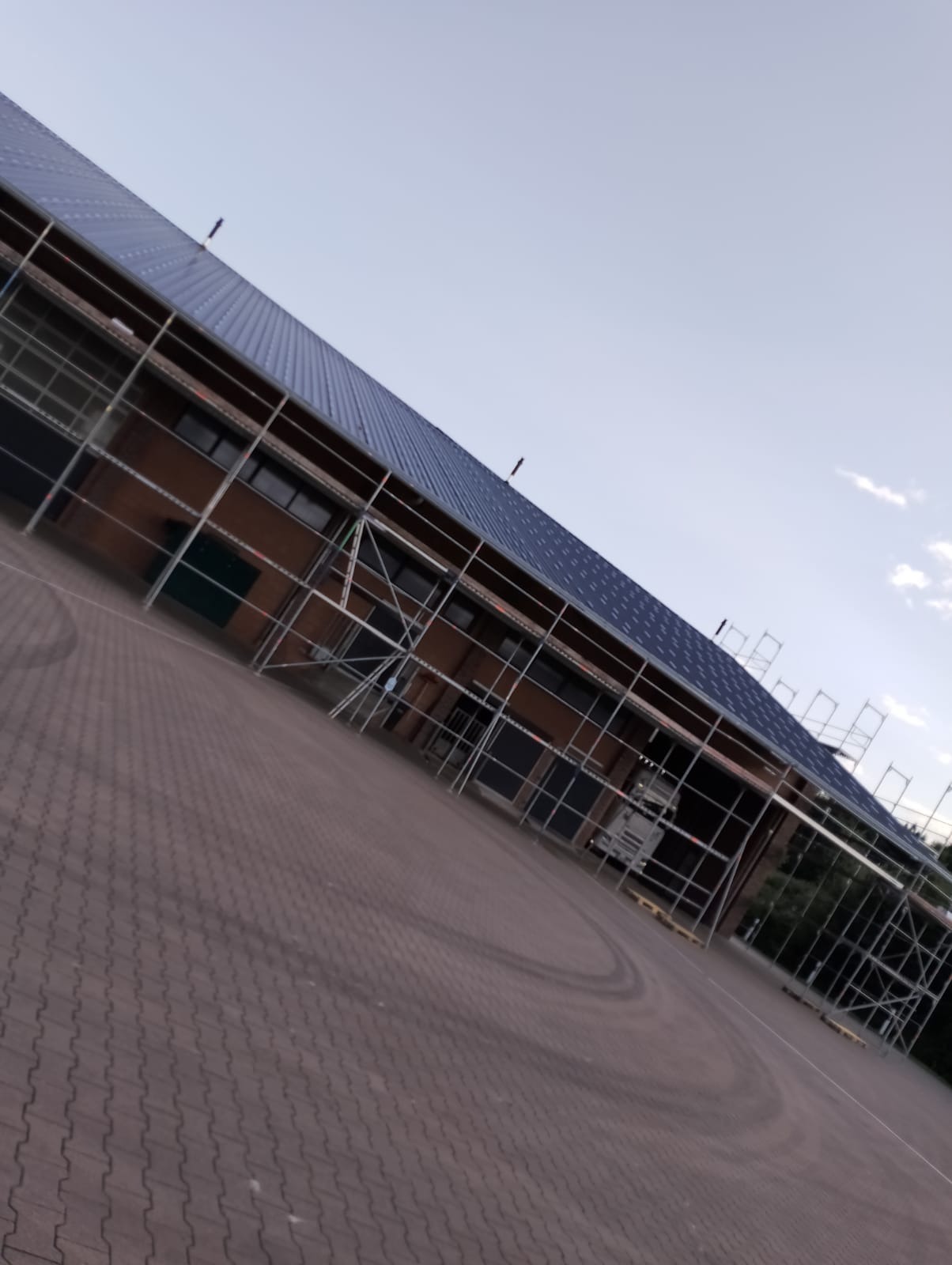 Budynek w trakcie montażu instalacji na dachu, widoczne rusztowania i częściowo zamontowane panele, z perspektywy ukośnej z ziemi.