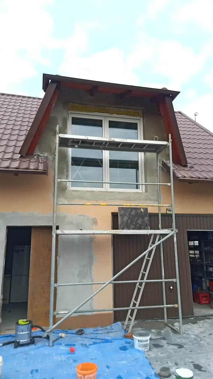 Dom z zamontowanym oknem, częściowo ocieplony, z ustawionym rusztowaniem i widocznym sprzętem budowlanym oraz częściowo zakrytą folią podłogą.