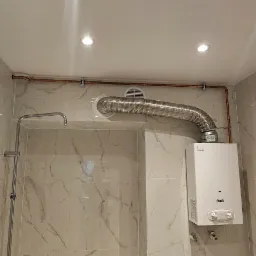 Biały piec gazowy Ferroli z podłączonym, elastycznym przewodem spalinowym w łazience wykończonej marmurowymi płytkami.