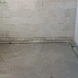 Surowy stan pomieszczenia z widocznymi przewodami elektrycznymi ułożonymi wzdłuż ścian i wyprowadzonymi gniazdkami podtynkowymi, ściany z bloczków betonowych, posadzka betonowa.