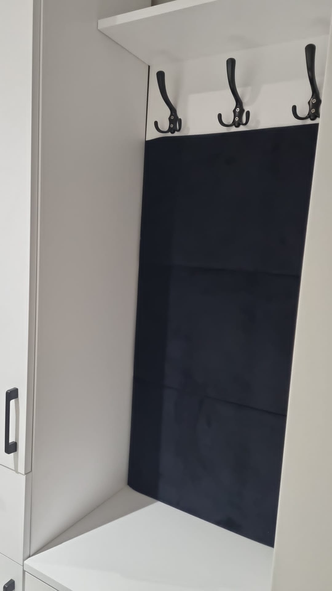 Biała szafa z wnęką i trzema czarnymi haczykami nad ciemnoniebieskim panelem.