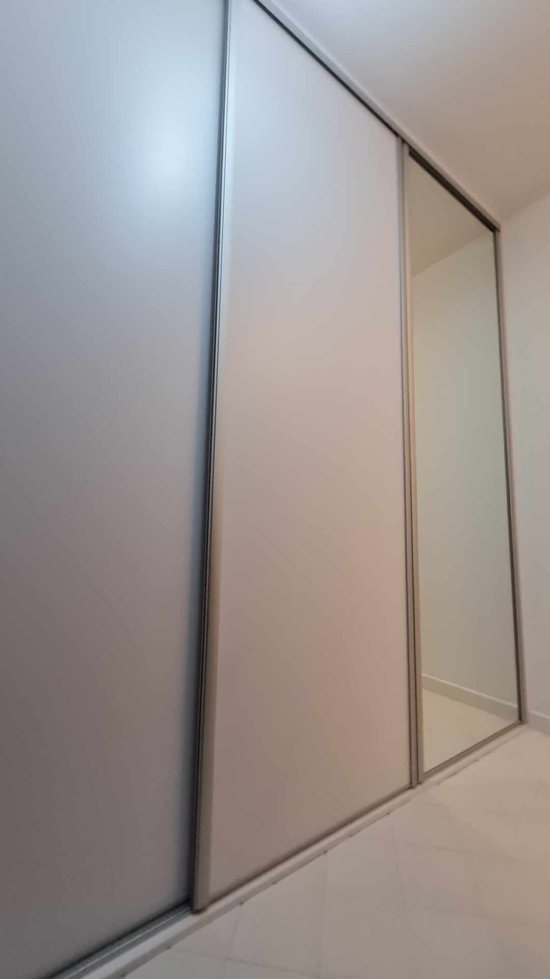 Minimalistyczna szafa przesuwna z szarymi frontami i lustrem, widok z dołu, srebrne obramowania, biała podłoga.