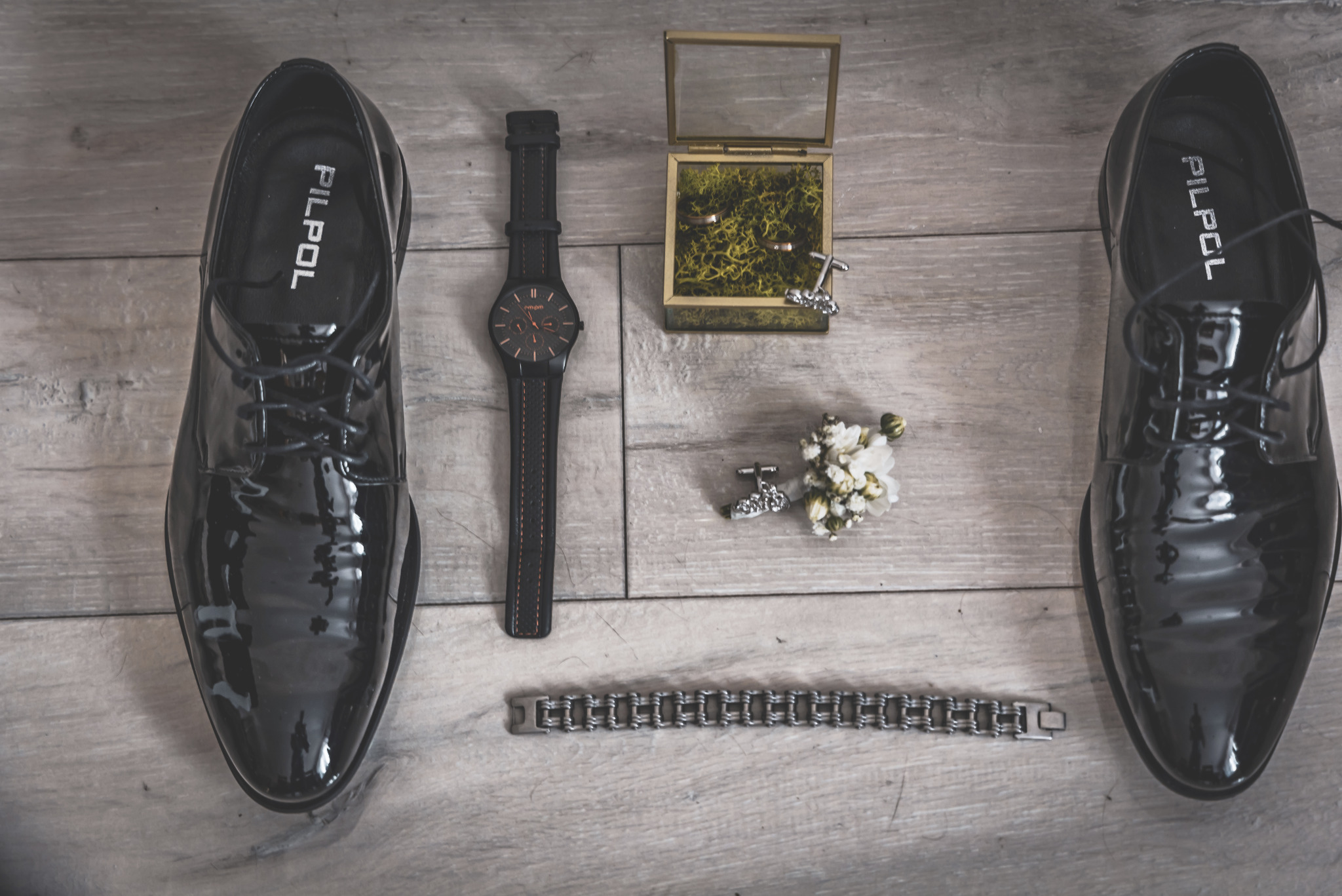 Eleganckie męskie akcesoria ślubne: lakierowane buty Pilpol, zegarek na skórzanym pasku z pomarańczowymi przeszyciami, spinki do mankietów, pudełko z obrączkami na mchu i bransoletka z ogniw...
