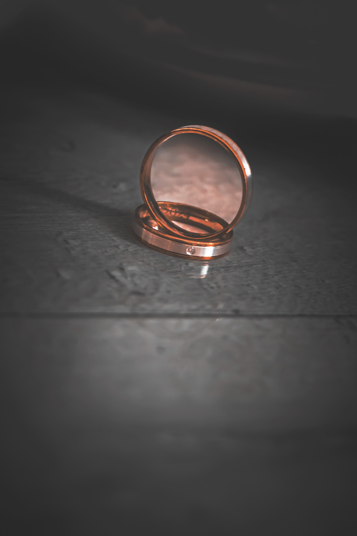 Dwa rose gold pierścionki ślubne z małym brylantem, ułożone jeden na drugim na ciemnym, drewnianym tle w minimalistycznym ujęciu z góry.