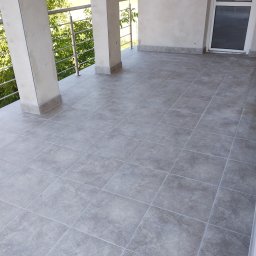 Euro styl wykończenia wnętrz Stanisław Moskwa - Szare płytki gresowe ułożone na balkonie z metalową balustradą i widokiem na zieleń, wykończenie z szarymi cokołami.